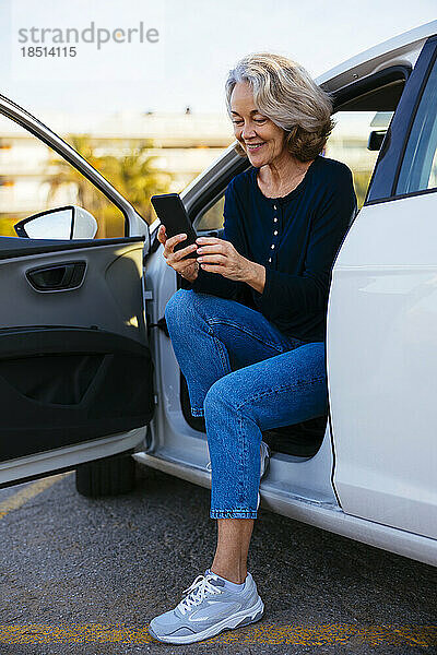 Lächelnde Frau  die im Auto sitzt und ihr Handy benutzt