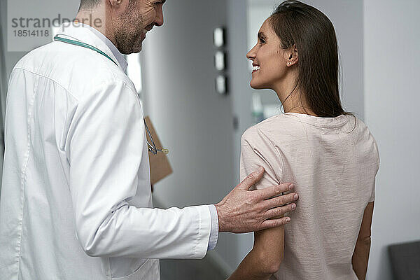 Glücklicher Arzt  der mit dem Patienten in der Klinik spricht
