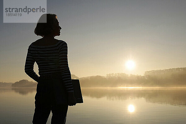 Silhouette eines Freiberuflers  der mit Laptop vor dem See steht