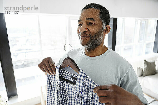 Smiling mature man trying on shirt at home