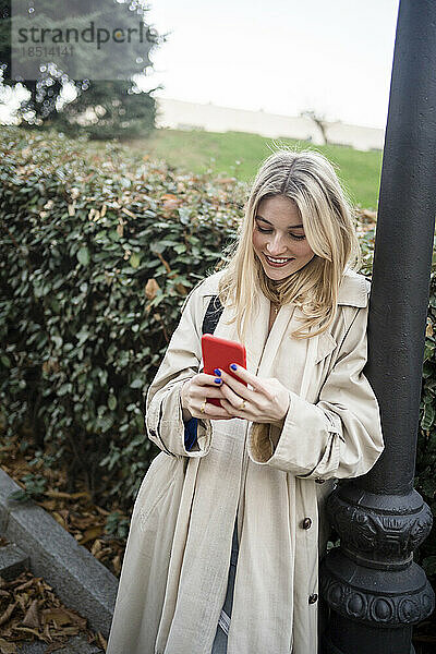 Lächelnde Frau benutzt Smartphone und stützt sich auf eine Stange