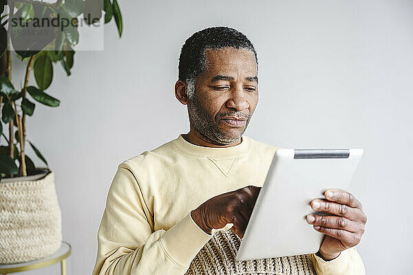 Mann sitzt zu Hause mit Tablet-PC vor der Wand