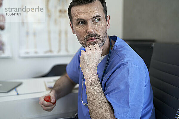 Nachdenklicher Arzt mit Stressball sitzt in der Klinik