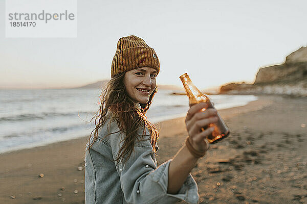 Glückliche Frau mit Bierflasche steht am Strand