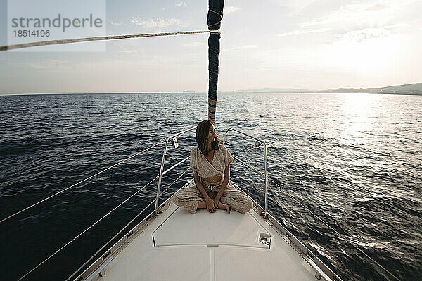 Frau sitzt auf einem Segelboot und genießt den Urlaub bei Sonnenuntergang