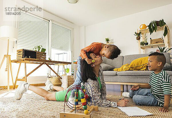 Verspielter Sohn küsst Mutter  die zu Hause auf dem Teppich liegt