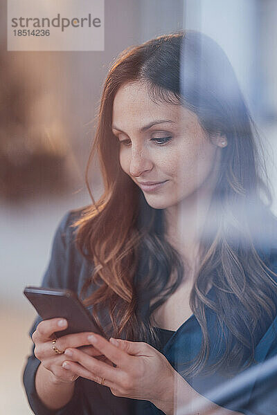 Junge Frau benutzt Smartphone  gesehen durch Glas