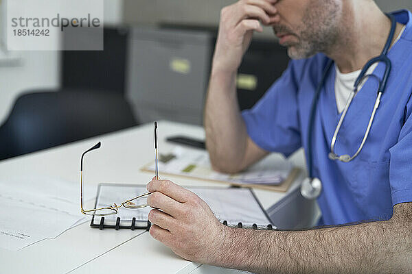 Müder reifer Arzt sitzt am Schreibtisch in der Klinik