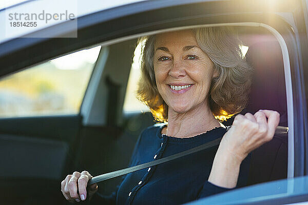 Glückliche reife Frau  die im Auto den Sicherheitsgurt anlegt