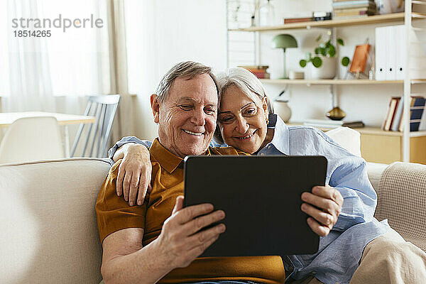 Glückliches älteres Paar  das zu Hause auf dem Sofa sitzt und auf einen Tablet-PC blickt