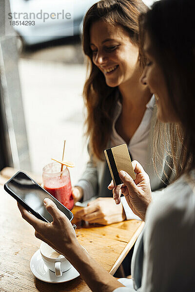 Frau hält Kreditkarte mit Smartphone von Freund im Café in der Hand