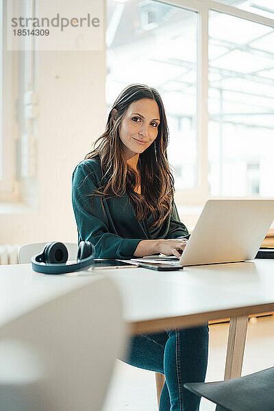 Lächelnde Geschäftsfrau sitzt mit Laptop im Heimbüro