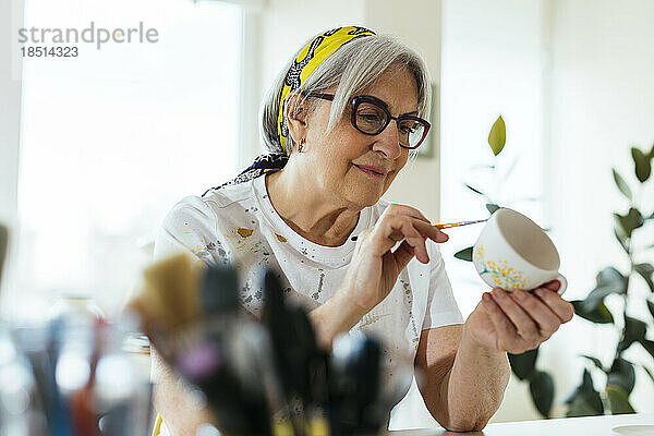Lächelnde Frau mit Brille bemalt Keramiktasse in Werkstatt