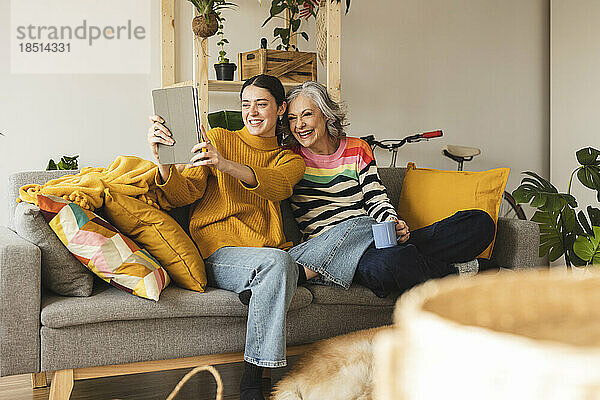 Glückliche Mutter mit Tochter  die zu Hause auf dem Sofa ein Selfie mit einem Tablet-PC macht