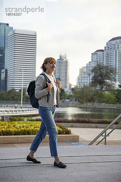 Reife Geschäftsfrau mit Rucksack geht auf Fußweg