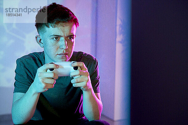 Young man holding controller playing video game at home