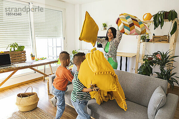 Playful mother playing pillow fight with twin sons at home