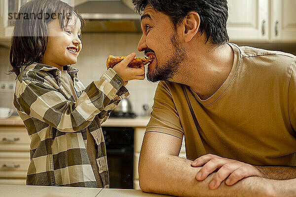 Glücklicher Junge  der seinem Vater zu Hause Pizza füttert