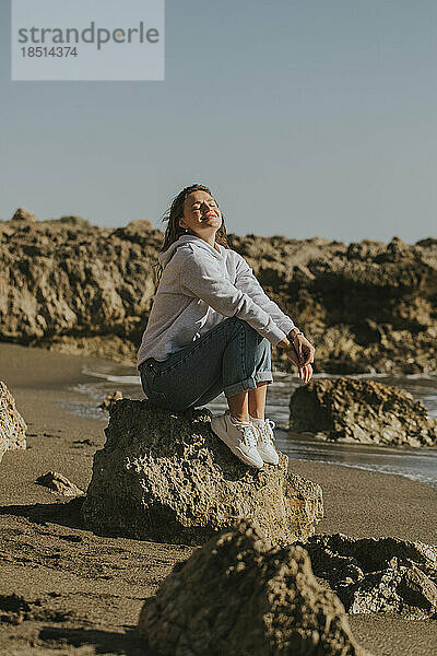 Frau sitzt auf einem Felsen am Strand