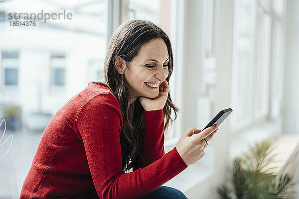 Glückliche Frau  die zu Hause mit dem Mobiltelefon im Internet surft