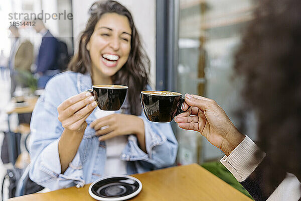 Fröhliche Freunde stoßen auf eine Kaffeetasse an und genießen sie im Straßencafé