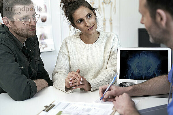 Smiling couple with doctor discussing over prescription in clinic