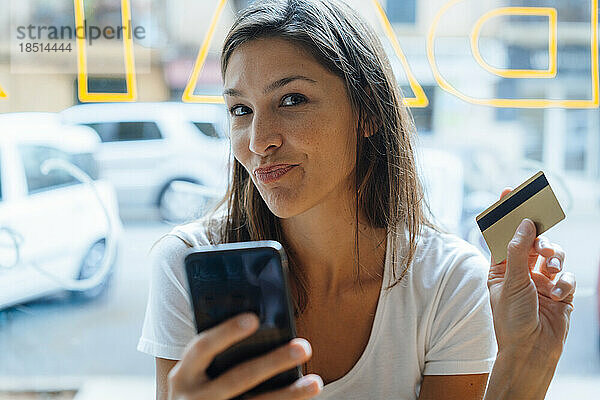 Frau mit Kreditkarte und Smartphone kräuselt sich im Café