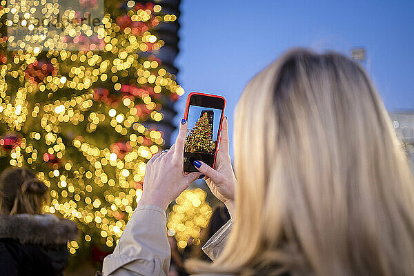 Frau fotografiert nachts beleuchteten Weihnachtsbaum per Smartphone