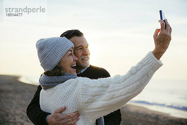 Happy mature woman taking selfie with man at beach