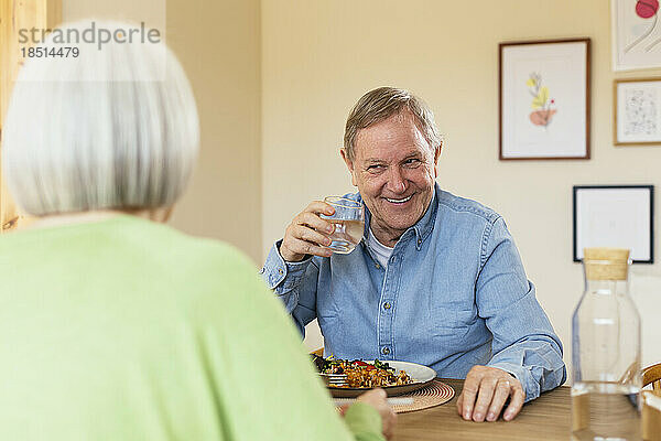 Lächelnder älterer Mann mit einem Glas Wasser  der zu Hause das Mittagessen genießt