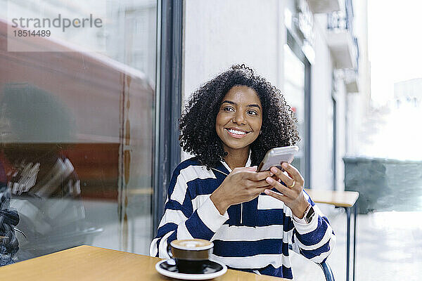 Glückliche Frau mit Smartphone sitzt am Tisch eines Straßencafés