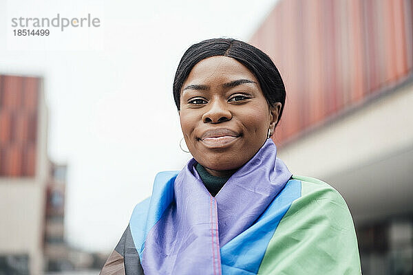 Lächelnde junge Frau in Regenbogenfahne gehüllt