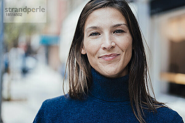 Lächelnde Frau mit braunem Haar und blauem Rollkragenpullover