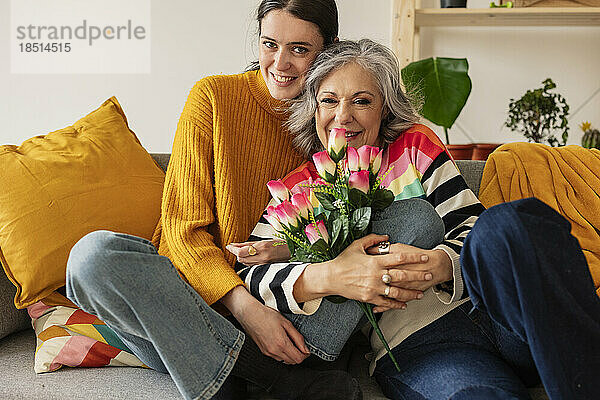 Glückliche Tochter mit Mutter  die zu Hause einen Blumenstrauß auf dem Sofa hält