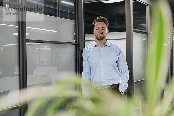 Young businessman standing by wall in office