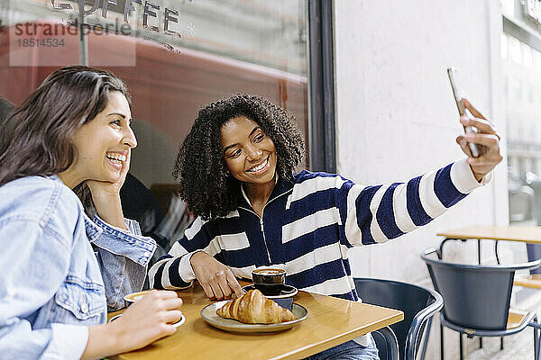 Lächelnde junge Frau macht ein Selfie mit einer Freundin im Straßencafé