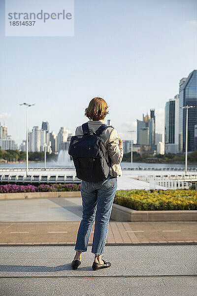 Geschäftsfrau mit Rucksack blickt auf Gebäude  die auf dem Fußweg stehen