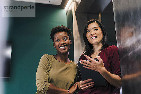 Glückliche Geschäftsfrauen stehen mit Tablet-PC im Büro