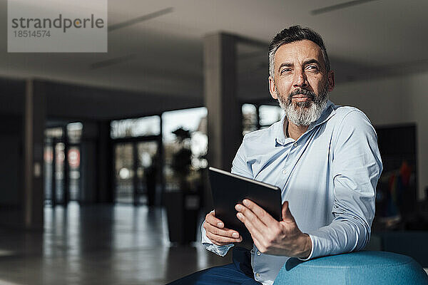 Nachdenklicher reifer Geschäftsmann sitzt mit Tablet-PC im Büro