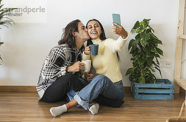 Happy man kissing girlfriend taking selfie at home
