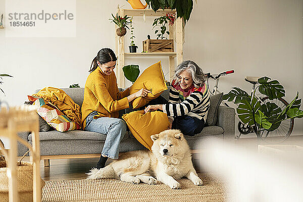 Playful mother and daughter holding cushion and looking at dog