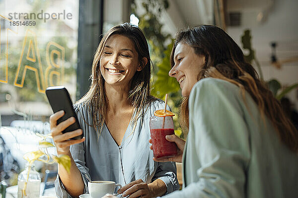 Glückliche Frau teilt Smartphone mit Freund im Café