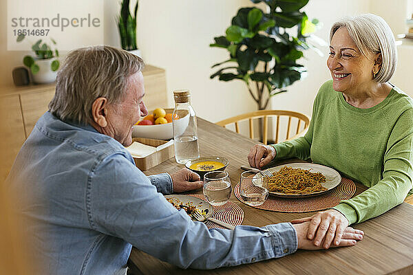 Glückliches älteres Paar mit gestapelten Händen beim Mittagessen zu Hause