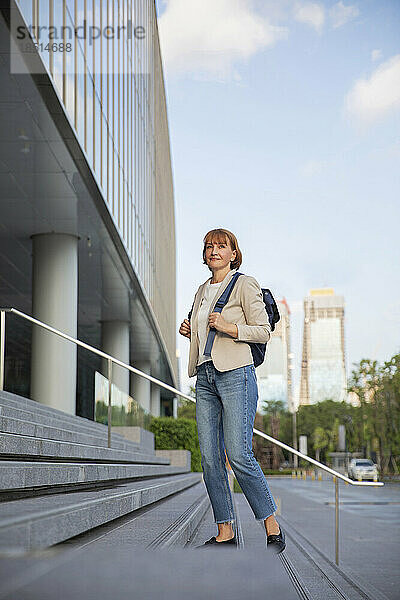 Reife Geschäftsfrau mit Rucksack steht auf Stufen