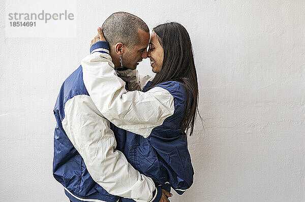 Liebevolles Paar umarmt sich vor einer weißen Wand