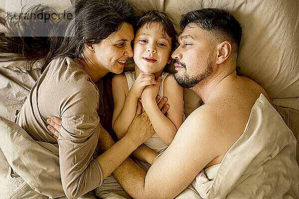 Happy parents lying with son on bed at home