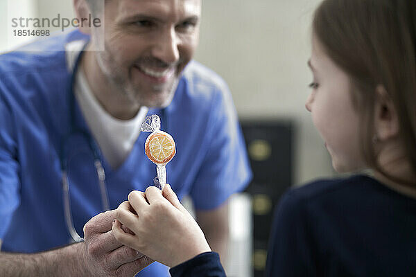 Happy doctor giving lollipop to girl in clinic