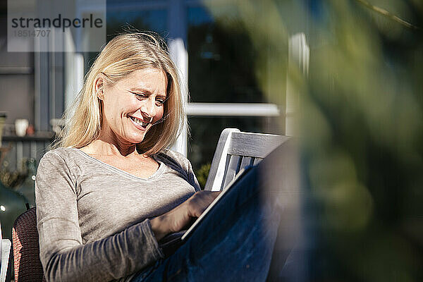 Lächelnder Freiberufler mit Tablet-PC  der an einem sonnigen Tag im Vorgarten sitzt