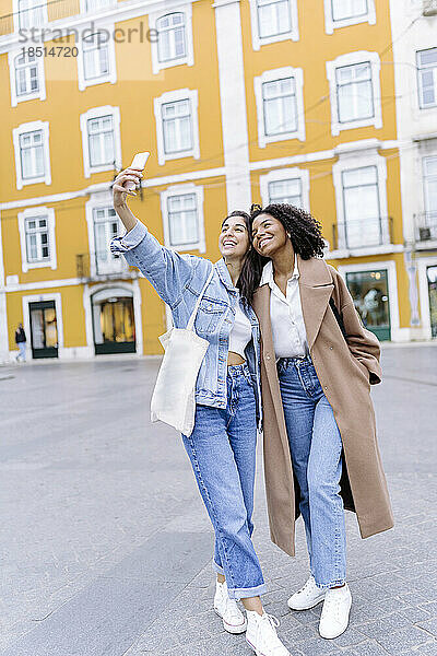 Fröhliche junge  gemischtrassige Freunde  die vor dem gelben Gebäude ein Selfie machen