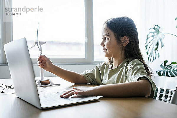 Mädchen mit Laptop berührt Windturbinenmodell auf Tisch zu Hause